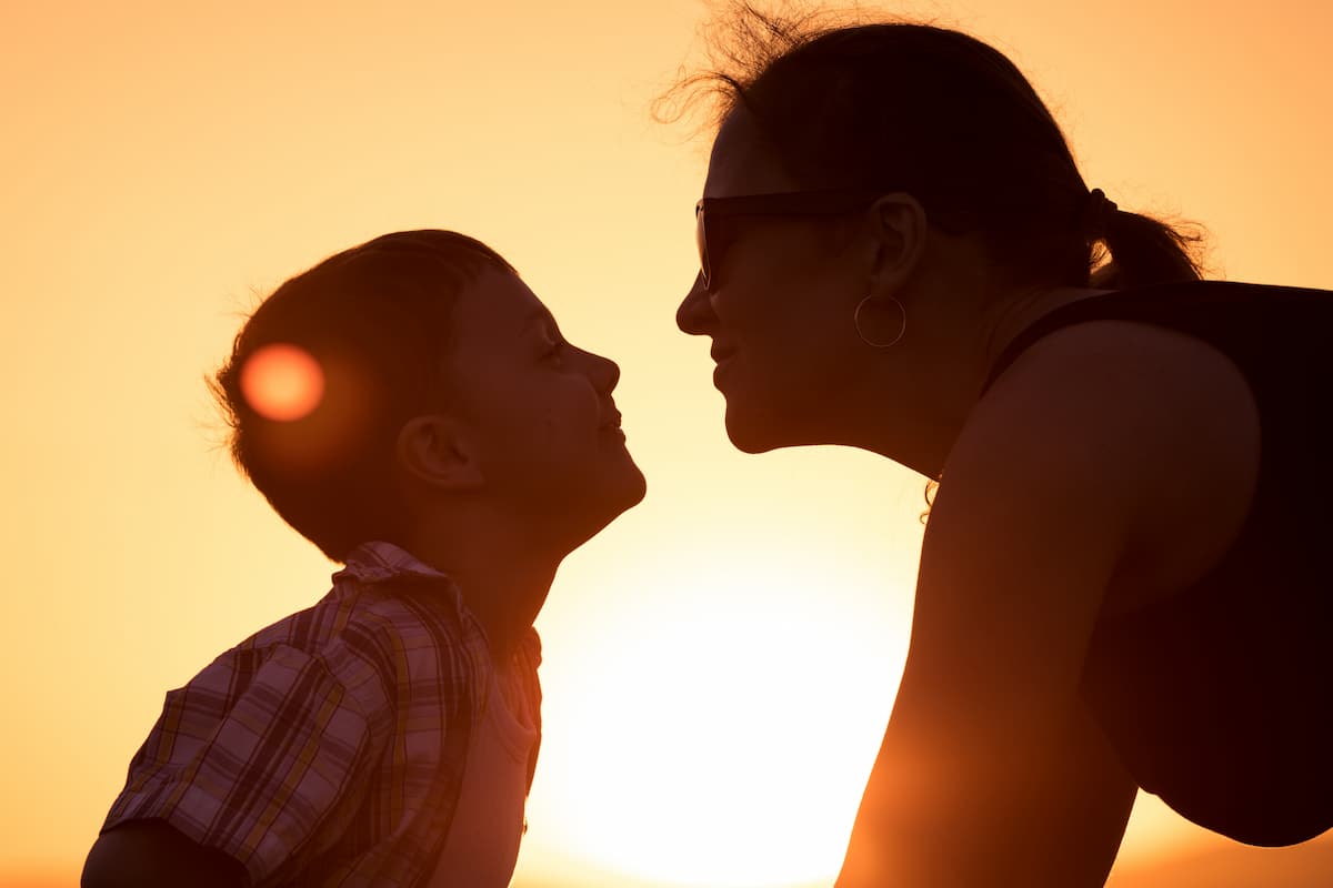 Mãe e filho sorriem ao pôr do sol e comunicam de forma consciente numa relação de parentalidade positiva