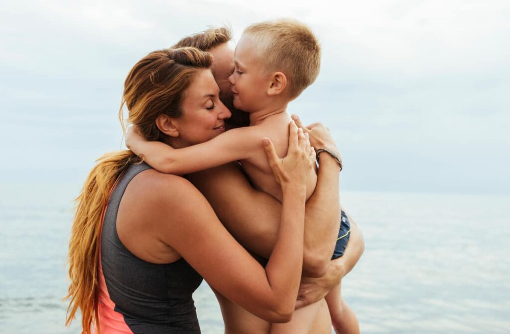 Um pai e uma mãe a abraçarem o filho na praia.